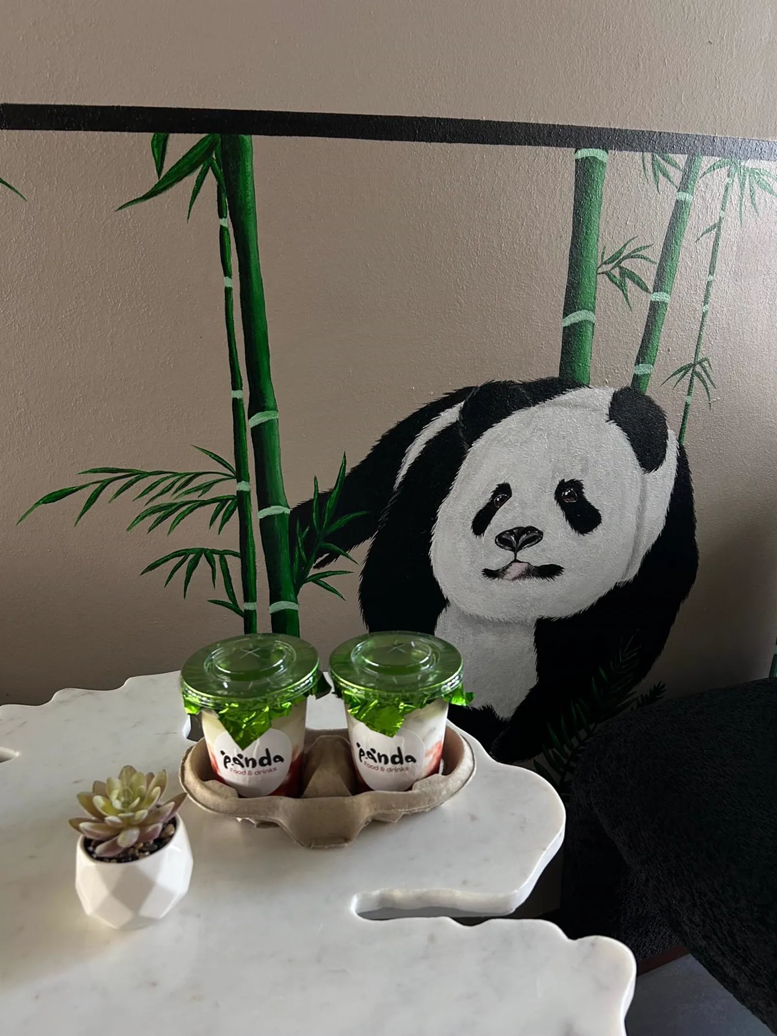 Zwei Desserts zum Mitnehmen vor dem gemalten Panda-Bambus-Wandbild